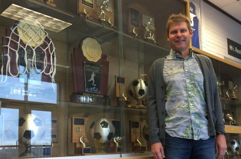 Coach Davidson stands next to the soccer trophies in the displace case in the entrance to the Eagle Gym.